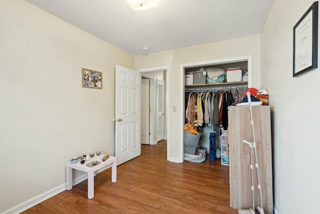 bedroom featuring a textured ceiling, a closet, wood finished floors, and baseboards