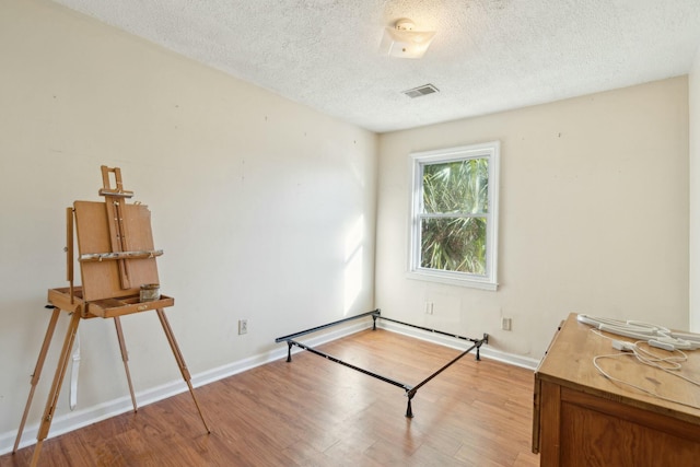 interior space featuring baseboards, light wood-style flooring, visible vents, and a textured ceiling