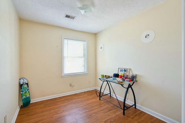 office featuring visible vents, a textured ceiling, baseboards, and wood finished floors