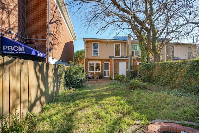 rear view of house with a fire pit, brick siding, fence, a lawn, and stucco siding