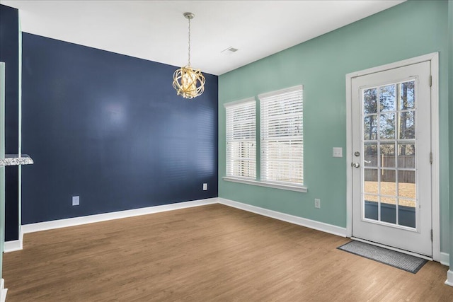 empty room featuring plenty of natural light, wood-type flooring, and an inviting chandelier