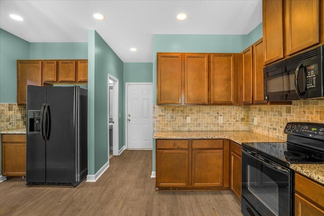 kitchen with backsplash, light stone countertops, light hardwood / wood-style flooring, and black appliances