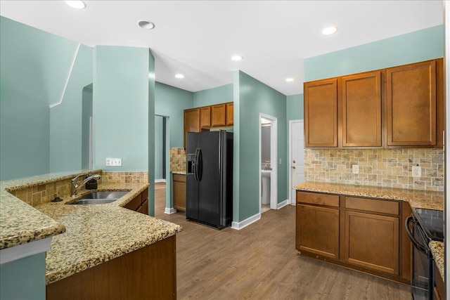 kitchen with black appliances, sink, hardwood / wood-style flooring, light stone countertops, and kitchen peninsula