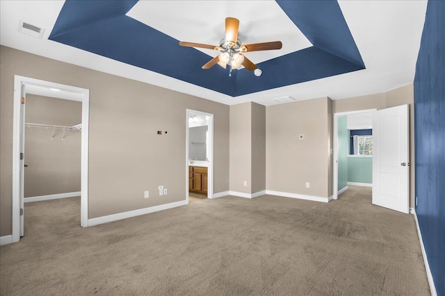 unfurnished bedroom featuring a raised ceiling, ensuite bath, ceiling fan, a spacious closet, and a closet