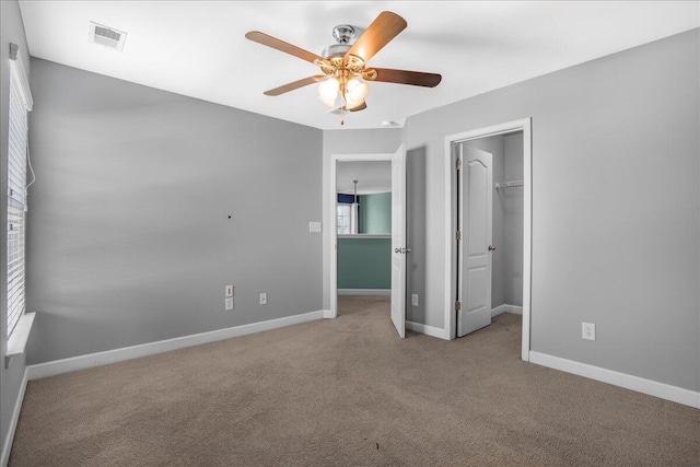 unfurnished bedroom featuring a closet, a walk in closet, light colored carpet, and ceiling fan