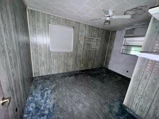 838 Ranch Hill Ln, Saint Stephen, SC 29479 - spare room featuring unfinished concrete flooring, a ceiling fan, and wood walls