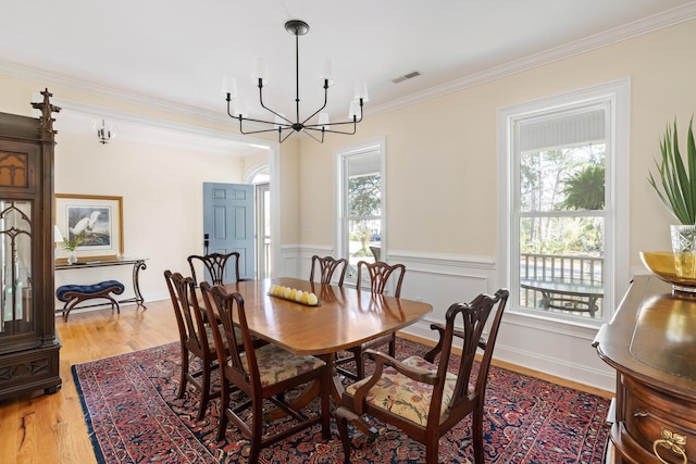 dining room featuring visible vents, wainscoting, light wood-style flooring, an inviting chandelier, and crown molding