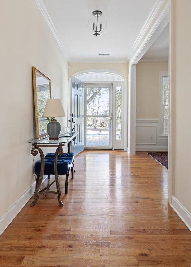 entrance foyer with visible vents, baseboards, a wainscoted wall, wood finished floors, and crown molding