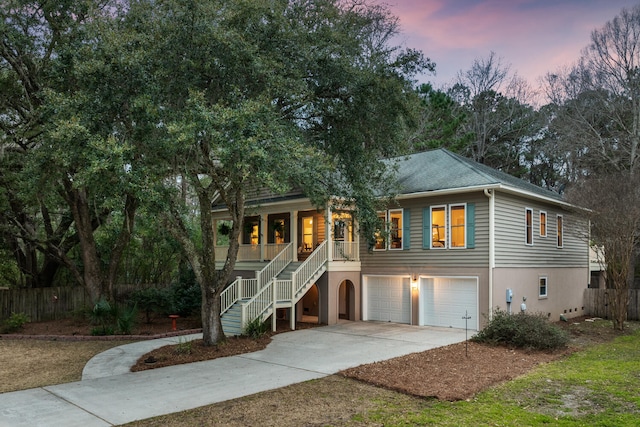 beach home with concrete driveway, stairway, an attached garage, a porch, and stucco siding