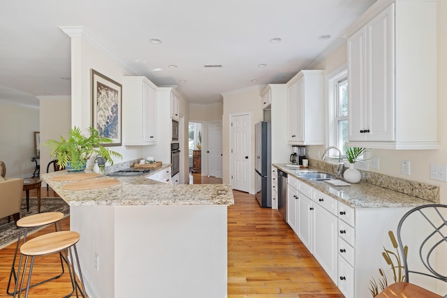 kitchen with light wood finished floors, a breakfast bar area, a peninsula, stainless steel appliances, and a sink