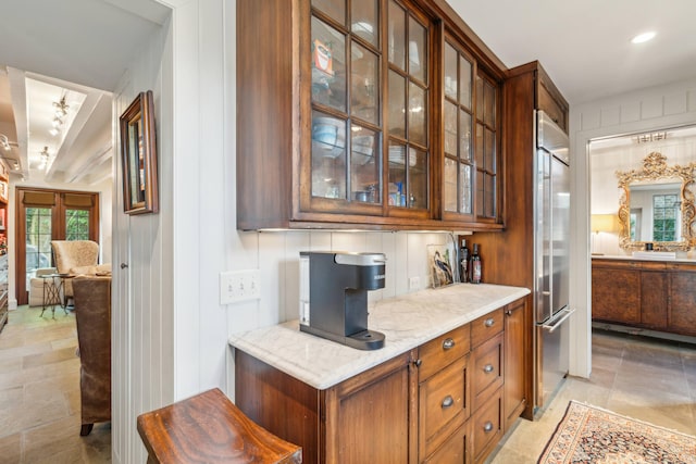 bar featuring stainless steel built in fridge, tasteful backsplash, and light stone counters