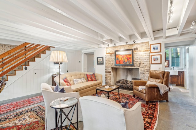 living room featuring beam ceiling, sink, and a brick fireplace