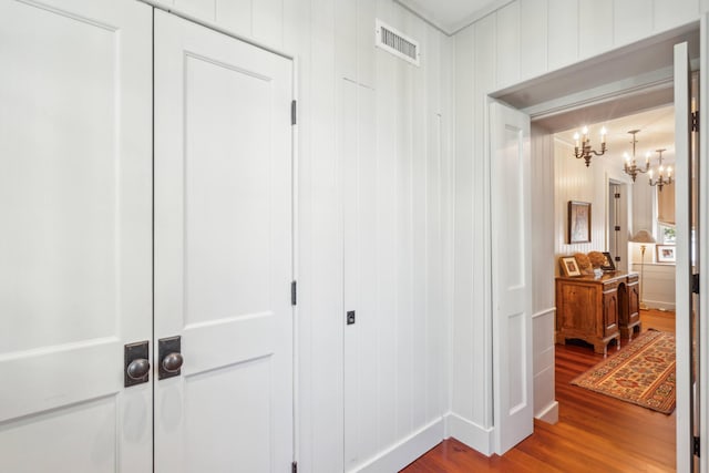 hall with hardwood / wood-style floors, wooden walls, and an inviting chandelier