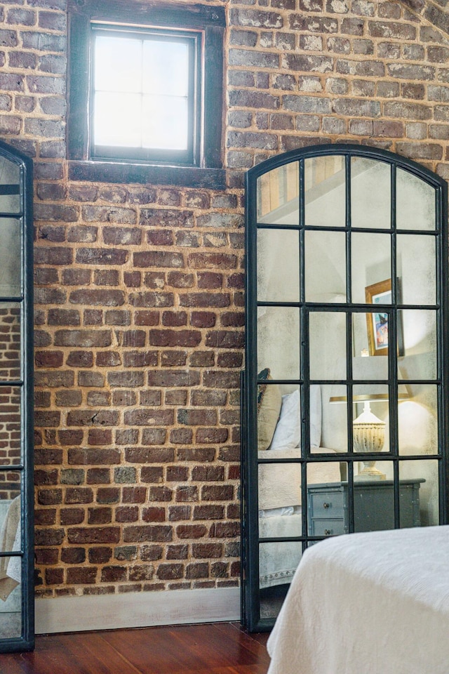 unfurnished bedroom with dark wood-type flooring and brick wall