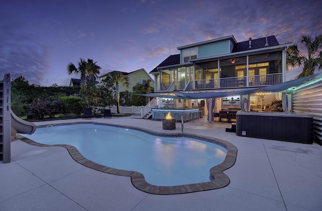 pool at dusk with stairway, a hot tub, a sunroom, a patio area, and a water slide