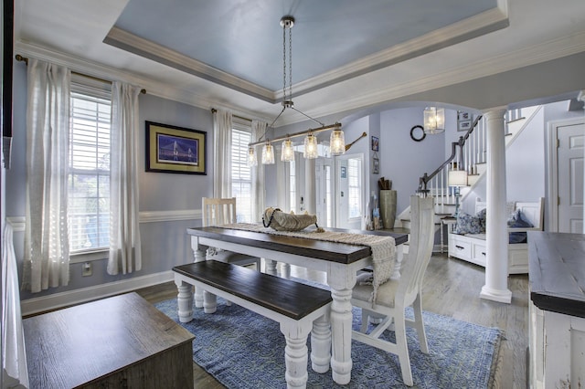 dining room with a tray ceiling, decorative columns, arched walkways, and stairs