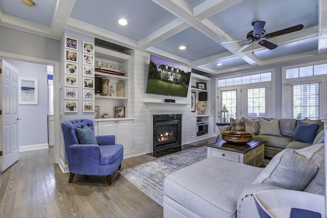 living area with a high end fireplace, beam ceiling, coffered ceiling, and wood finished floors