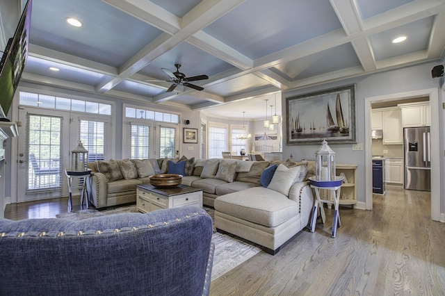 living area featuring ceiling fan with notable chandelier, beamed ceiling, light wood-type flooring, and coffered ceiling