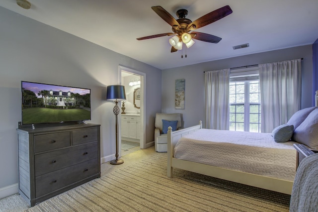 bedroom featuring ceiling fan, light colored carpet, visible vents, baseboards, and ensuite bath