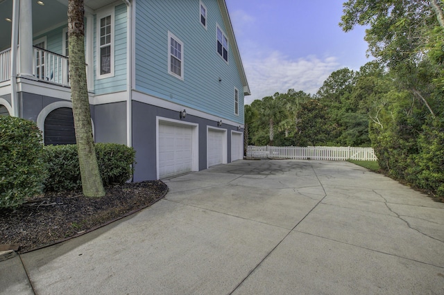 view of property exterior featuring an attached garage, a balcony, fence, driveway, and stucco siding