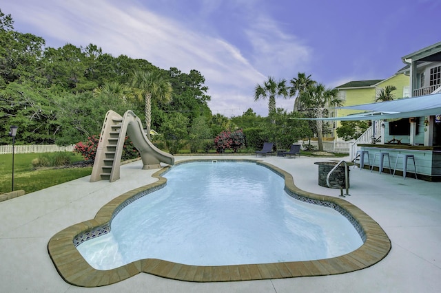 view of swimming pool with outdoor dry bar, a water slide, a patio area, and a fenced backyard