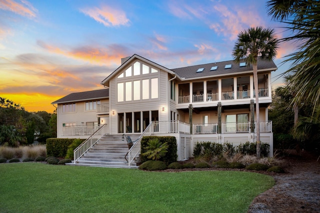 back of property at dusk featuring a balcony, a chimney, stairway, and a yard