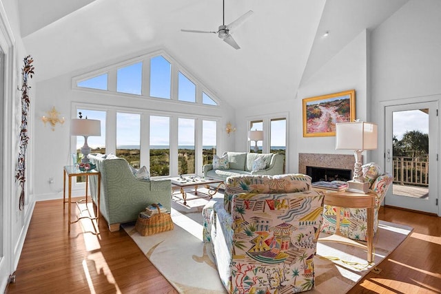 living area featuring high vaulted ceiling, a ceiling fan, a fireplace, and wood finished floors