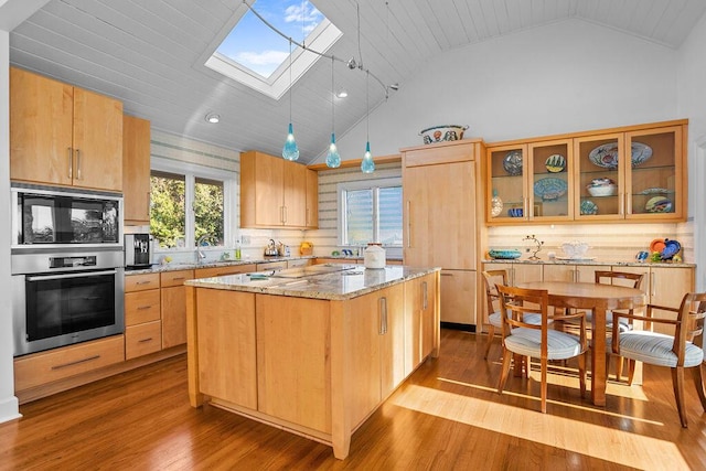 kitchen featuring a skylight, a center island, a sink, light stone countertops, and built in appliances