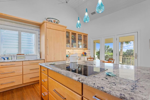 kitchen with light stone counters, decorative backsplash, glass insert cabinets, wood finished floors, and black electric cooktop