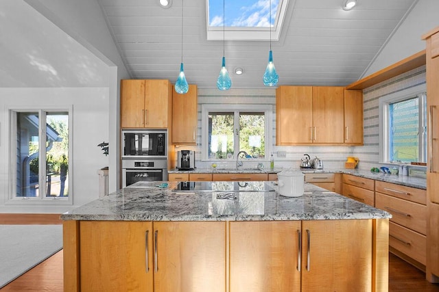 kitchen with black appliances, vaulted ceiling with skylight, a sink, and light stone countertops