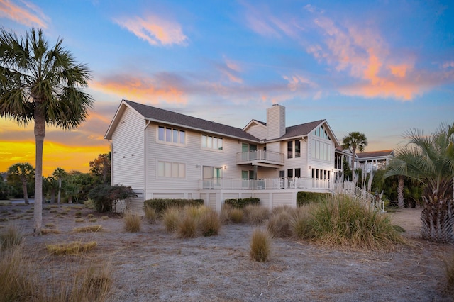 back of house at dusk with a balcony and a chimney