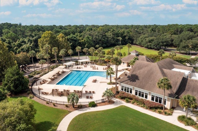 community pool with a yard, a patio area, fence, and a forest view