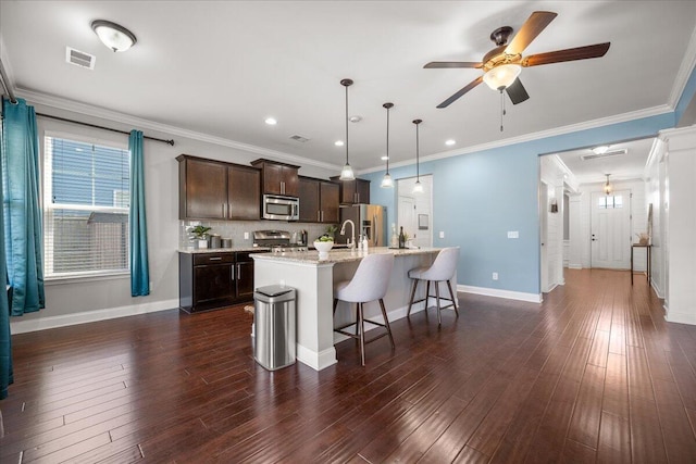 kitchen with a center island with sink, stainless steel appliances, dark brown cabinetry, decorative light fixtures, and a kitchen bar