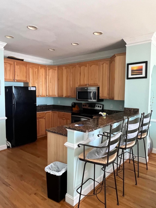 kitchen featuring kitchen peninsula, a breakfast bar, dark stone counters, light hardwood / wood-style flooring, and stainless steel appliances