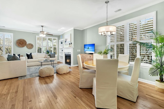 dining space with light hardwood / wood-style floors, ceiling fan with notable chandelier, a healthy amount of sunlight, and ornamental molding