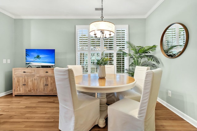 dining space with light hardwood / wood-style floors, ornamental molding, and an inviting chandelier