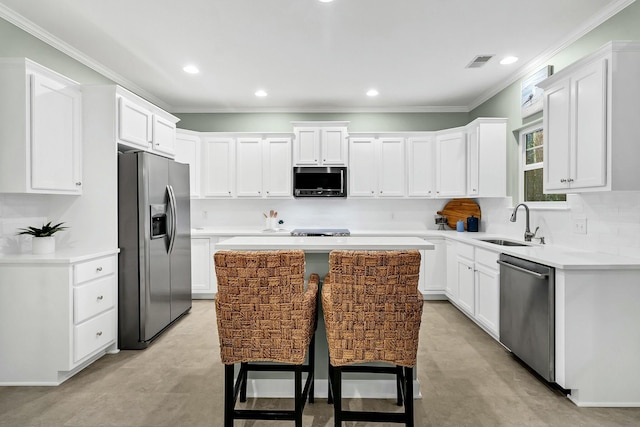 kitchen with appliances with stainless steel finishes, a kitchen breakfast bar, sink, white cabinets, and a kitchen island