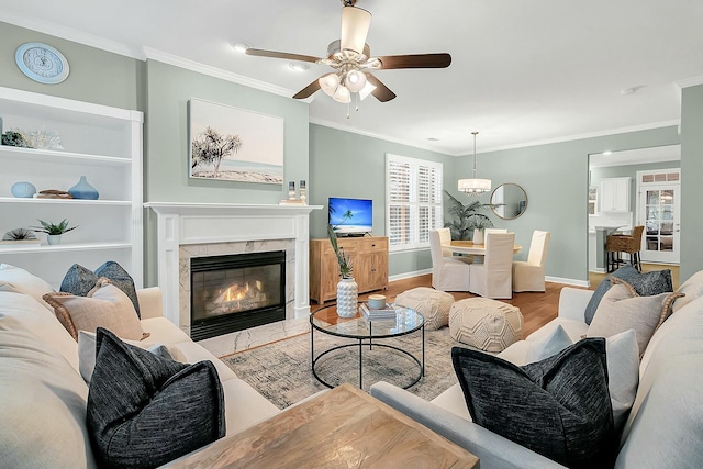 living room with light hardwood / wood-style flooring, a high end fireplace, ceiling fan with notable chandelier, and ornamental molding