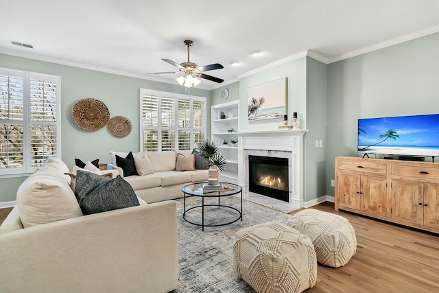 living room with ornamental molding, ceiling fan, built in features, light hardwood / wood-style flooring, and a premium fireplace