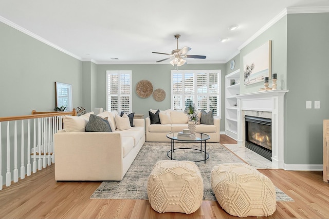 living room with light wood-type flooring, ceiling fan, crown molding, built in features, and a fireplace