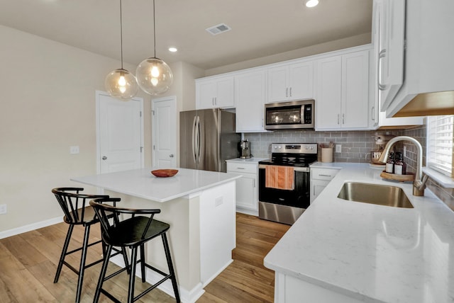 kitchen with stainless steel appliances, a sink, a breakfast bar area, a kitchen island, and light wood-style floors