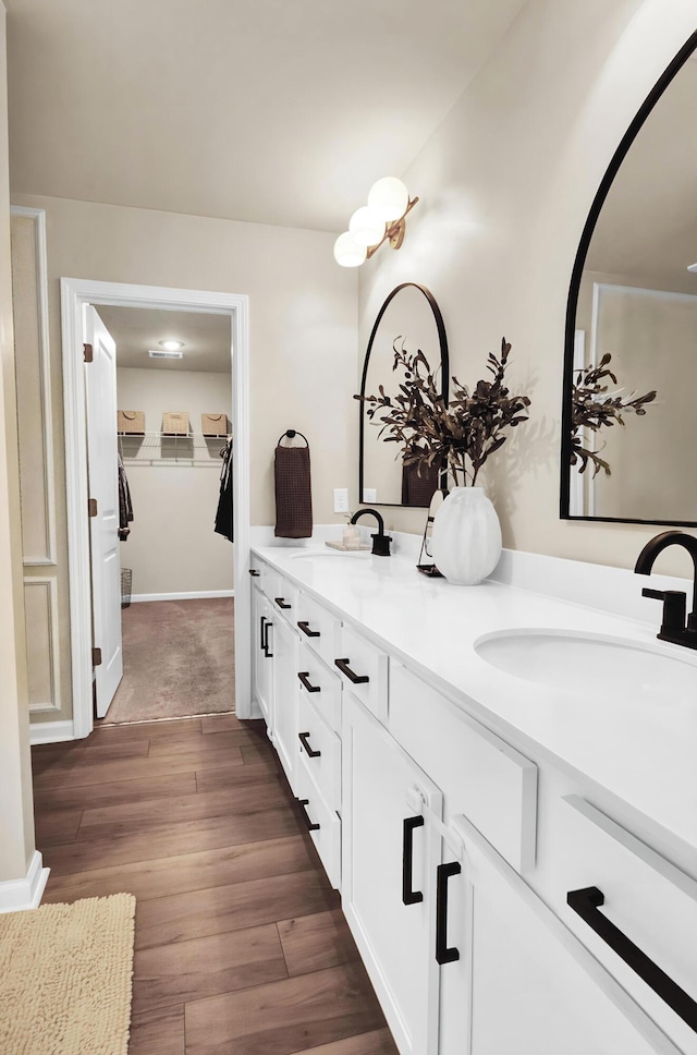 bathroom featuring wood finished floors, double vanity, a walk in closet, and baseboards