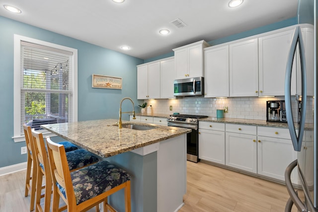 kitchen featuring light wood-type flooring, backsplash, visible vents, appliances with stainless steel finishes, and a sink