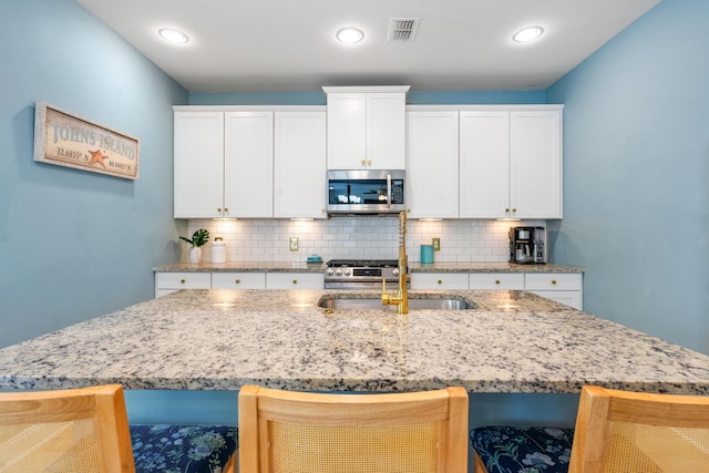kitchen with visible vents, a breakfast bar, a sink, stainless steel appliances, and backsplash