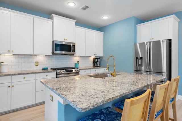 kitchen with appliances with stainless steel finishes, light wood finished floors, a sink, and visible vents