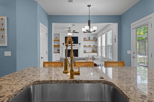 kitchen featuring a fireplace, light stone countertops, visible vents, a sink, and decorative light fixtures