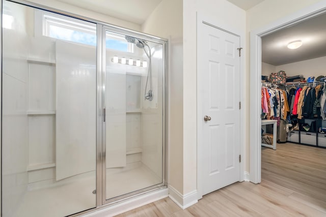 bathroom featuring a spacious closet, a shower stall, and wood finished floors
