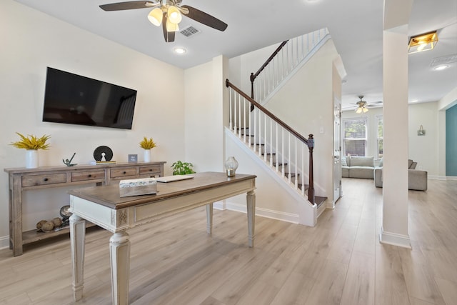 living room featuring light wood-type flooring, ceiling fan, visible vents, and stairs