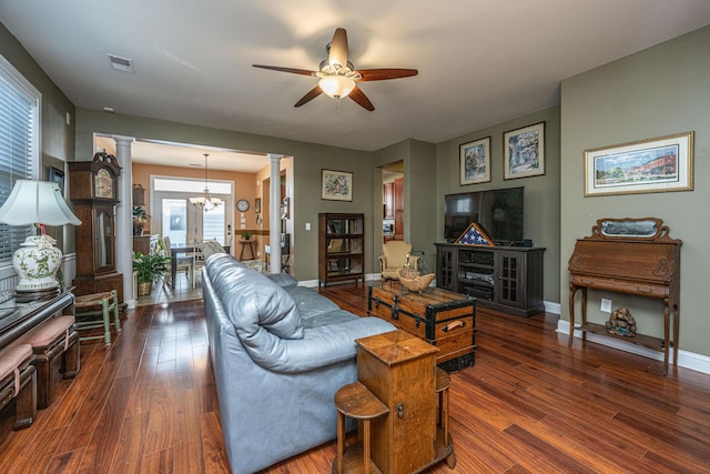 living room with ceiling fan with notable chandelier, dark hardwood / wood-style flooring, ornate columns, and plenty of natural light