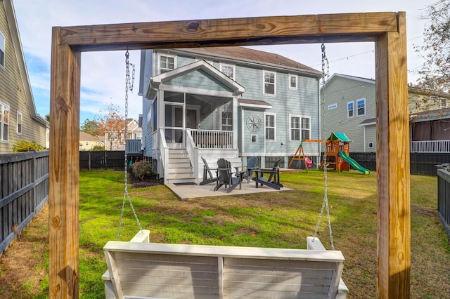 rear view of property featuring a sunroom, a patio area, a playground, and a lawn